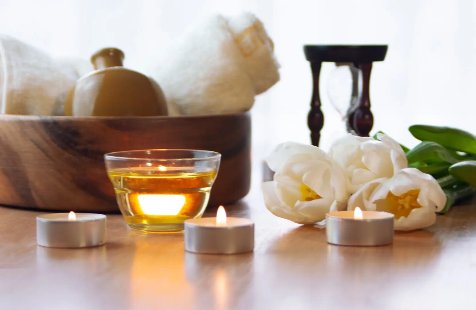 Glass candle holder with burning tea lights, white flowers, essential oils, and rolled towels arranged on a wooden surface—visualizing relaxation and holistic wellness at Chronic Health Wisdom