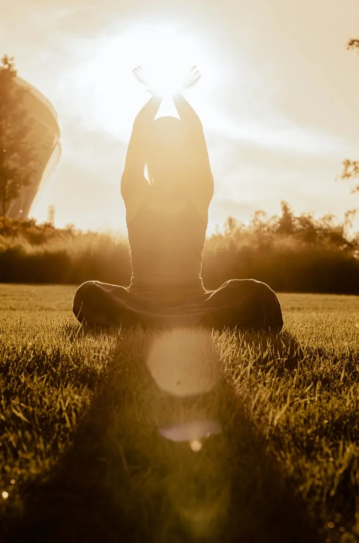Silhouette of a person with arms raised toward the sun in a golden outdoor landscape, representing gentle movement for fatigue support – Chronic Health Wisdom