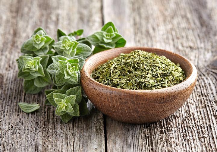 Oregano in a bowl on a wooden table.
